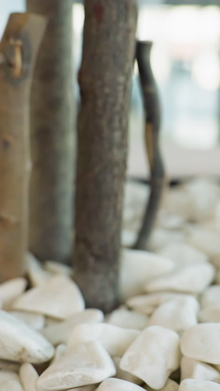 A close-up view of a decorative plant pot filled with white stones and tree branches or stems in a public indoor space. The background is blurred