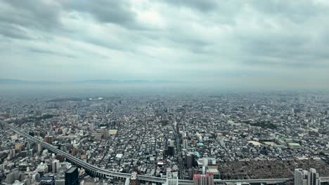 elevated highway curving through a dense cityscape in osaka, japan, with mountains visible in the distance under a cloudy sky