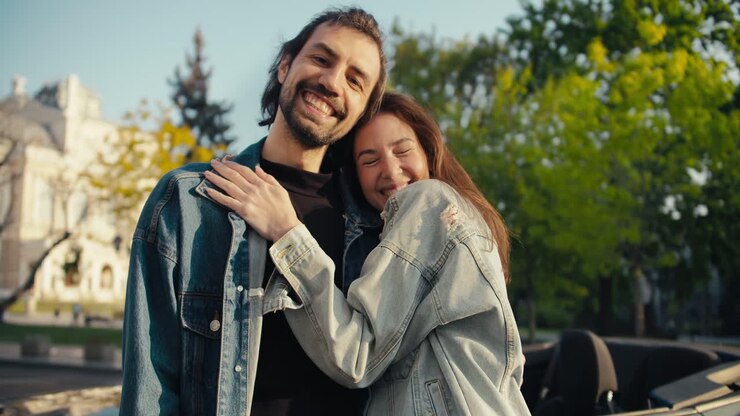 Close-up shot of a brunette girl kissing her boyfriend on the cheek on the street near their Gray Convertible, happy couple life