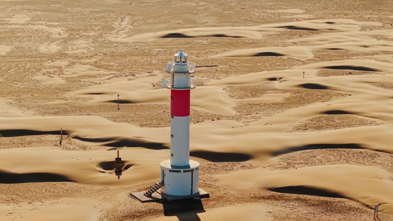 Faro di Fangar circondato da dune di sabbia modellate dal vento a Punta del Fangar nel Parco Naturale del Delta dell'Ebro, Spagna. Primo piano aereo con drone dell'iconico faro costiero.