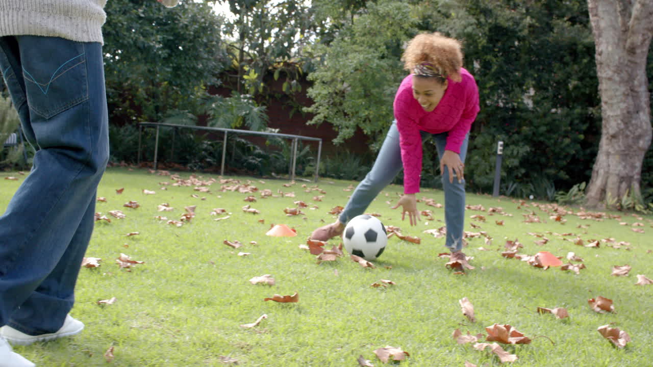 Happy african american mother and son in scarf lying on fallen leaves in garden, slow motion