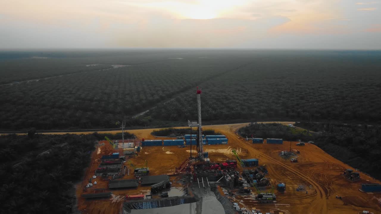 imágenes cinematográficas de drones de la estructura del equipo de la plataforma de perforación en tierra para la exploración y explotación de petróleo en medio de la jungla rodeada de palmeras durante la puesta de sol y el alto precio del petróleo