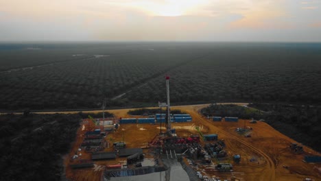 Cinematic-Drone-Footage-of-Onshore-Drilling-Rig-equipment-structure-for-oil-exploration-and-exploitation-in-the-middle-of-jungle-surrounded-by-palm-oil-trees-during-sunset-and-high-oil-price