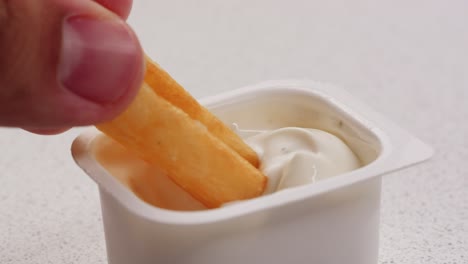 hand dipping french fries into a container of creamy sauce