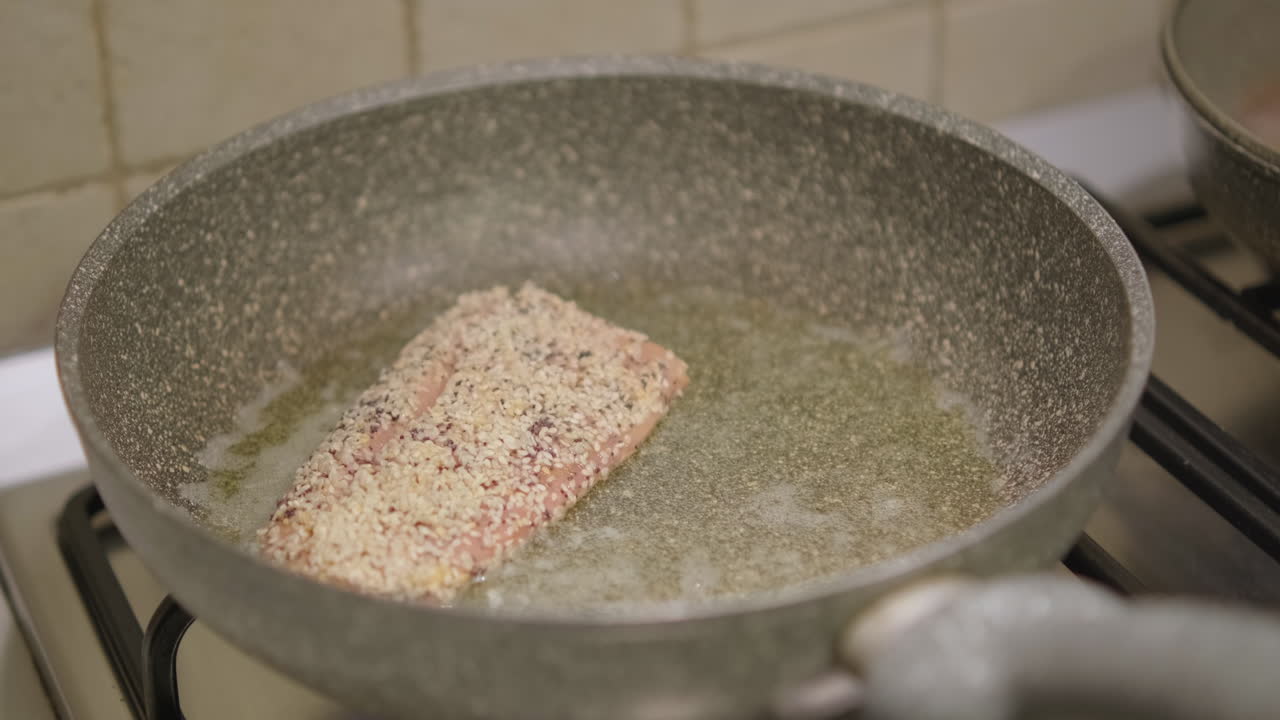primer plano, manos femeninas poniendo un trozo de carne de pescado de salmón con sabor en una sartén en la estufa en la cocina de casa, cámara lenta