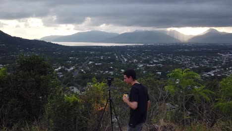 photographer walking away from his camera while drinking coffee on the top of a mountain