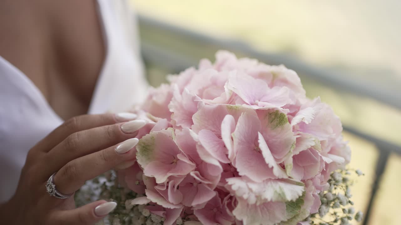 la novia acaricia suavemente un delicado ramo de hortensia rosa con uñas cuidadosas