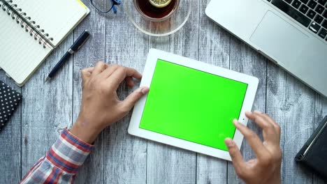 persona que utiliza una tableta con pantalla verde en un escritorio de madera