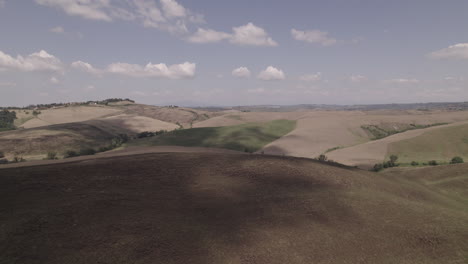 fotografía de avión no tripulado de carreteras sinuosas y campos agrícolas dorados en la toscana, italia paisaje en un día soleado con cielo azul y nubes en el horizonte proyectando un tronco de sombra en movimiento