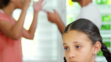 chica triste sentada en la mesa mientras los padres discuten en el fondo