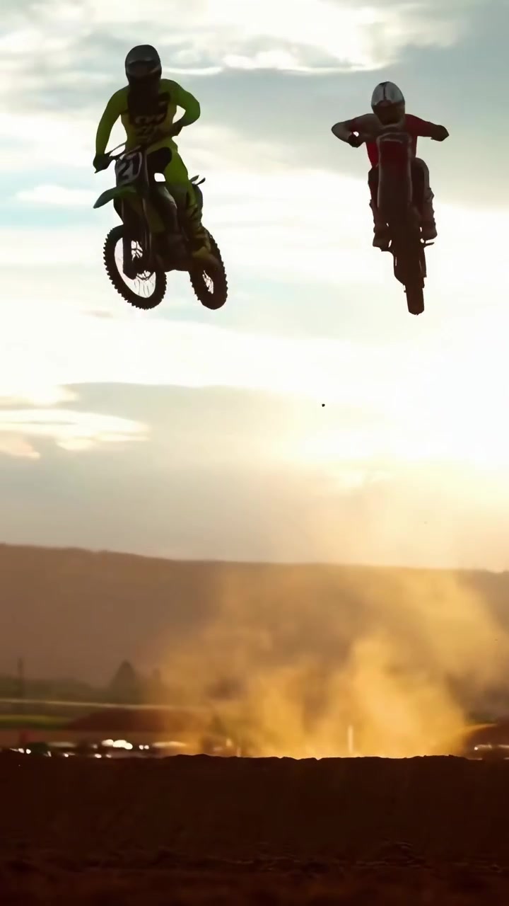 Dois Pilotos de Motocross Saltando Sobre uma Pista de Terra ao Pôr do Sol
