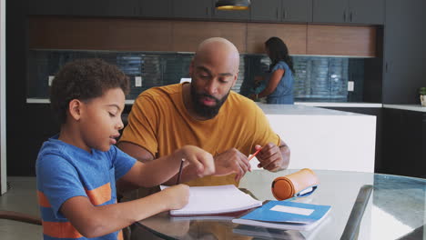 Padres-Afroamericanos-Ayudando-A-Su-Hijo-A-Estudiar-La-Tarea-En-La-Cocina