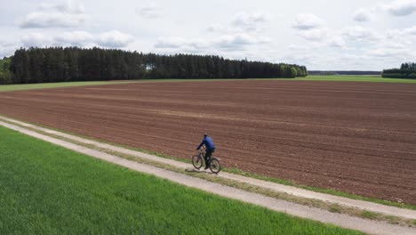 aerial wide shot of a man riding a bike on a small dirt road