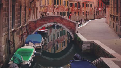 un canal veneciano con un puente entre las antiguas casas medievales en el centro de la ciudad antigua del famoso sitio del patrimonio de la unesco venecia en italia con aguas azules claras y barcos y embarcaciones en el lugar de vacaciones turísticas.