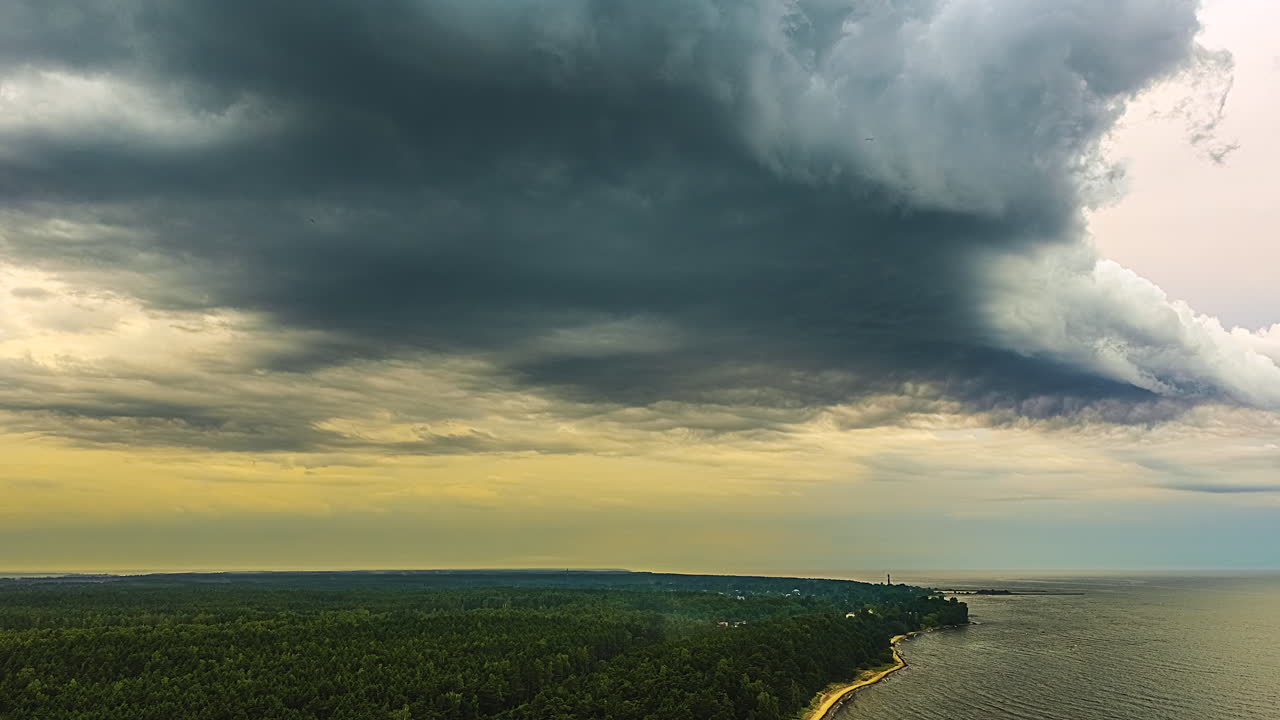 Dramatic time lapse shows dark storm clouds moving quickly over the Latvian coastline with a green forest and the Baltic Sea at sunset