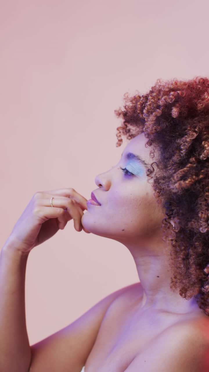 Vídeo vertical de mulher birracial com cabelo escuro em luz azul e rosa, em câmera lenta.