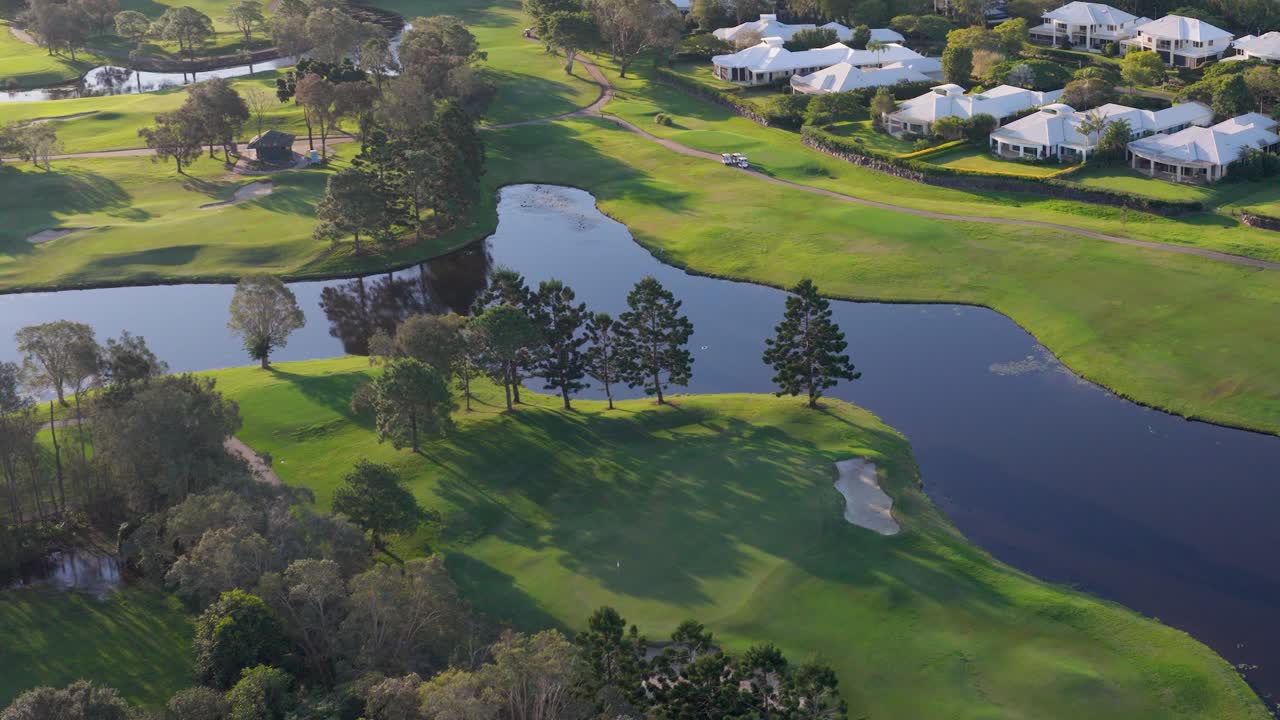 Drone captures lush golf course with water hazards and surrounding homes during golden sunset hour in Gold Coast, Australia
