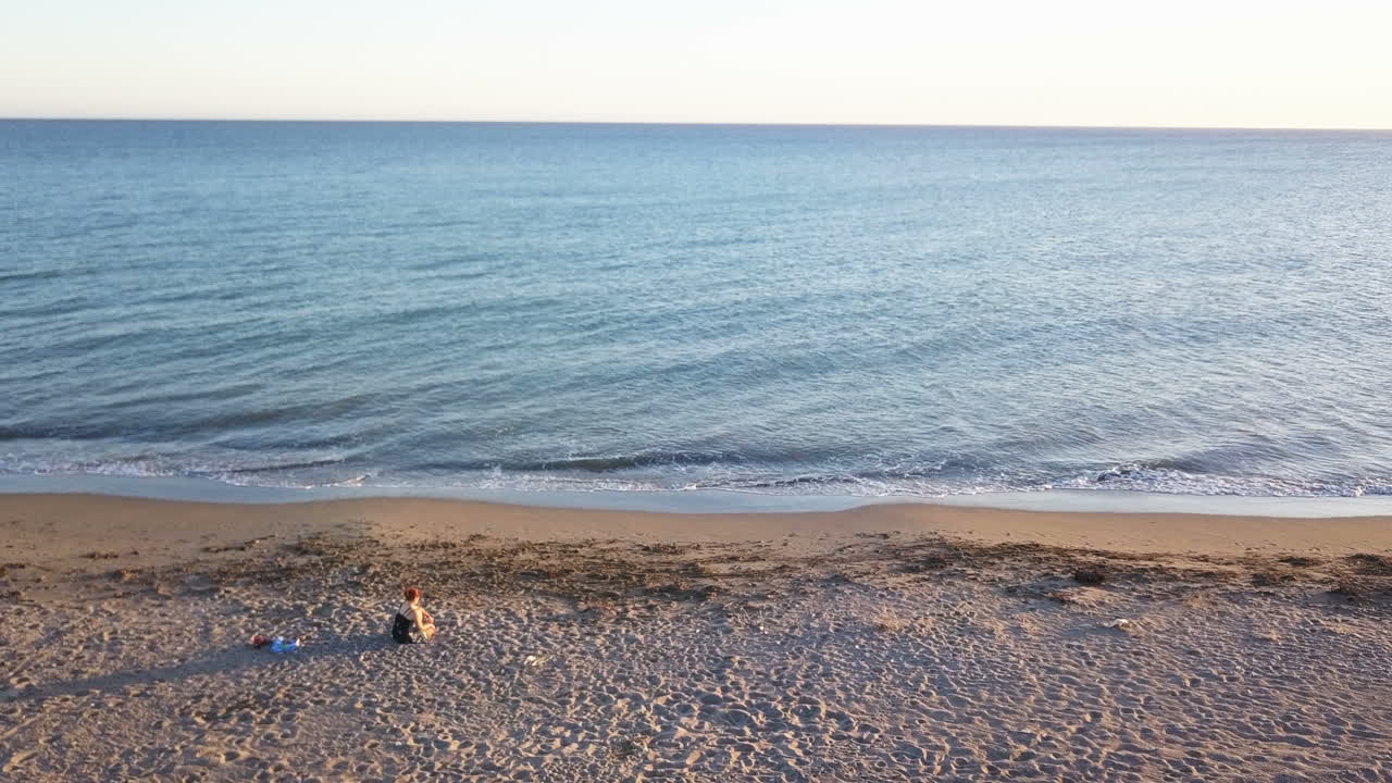 A tranquil beach scene with a person sitting on the sand by the ocean