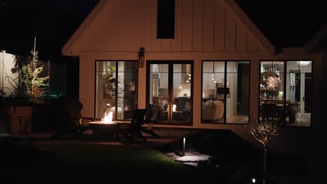 exterior home at night with firepit, flickering firelight on house, dimly lit living room visible