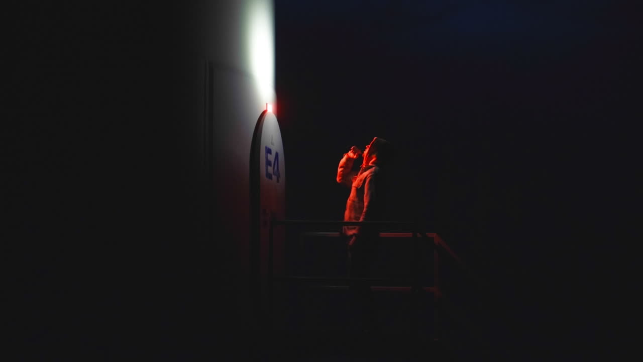vista lateral de un hombre siniestro con linterna llegando a la puerta de un edificio extraño por la noche