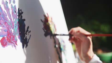 Midsection-of-caucasian-woman-painting-in-sunny-garden