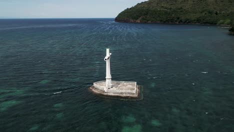 White-Cross-monument-at-Sunken-Cemetery-near-shore-of-Camiguin,-aerial