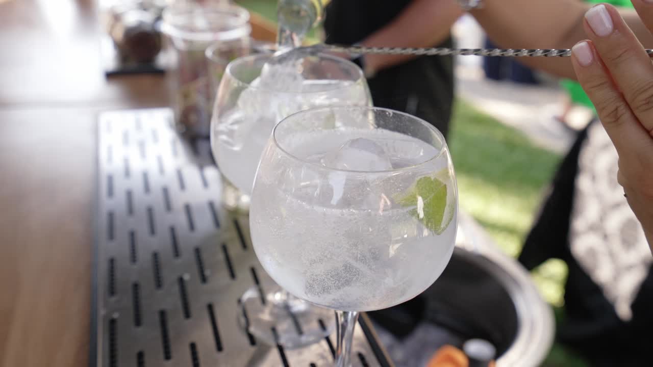 Close up of gin and tonic being poured over ice with lime garnish outdoors