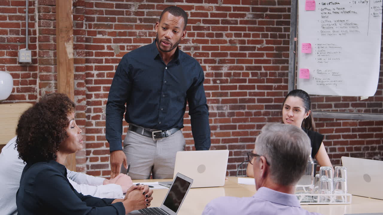 Businessman Leading Office Meeting Of Colleagues Sitting Around Table