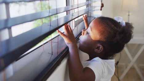 Niña-Afroamericana-Mirando-Por-La-Ventana-En-Casa