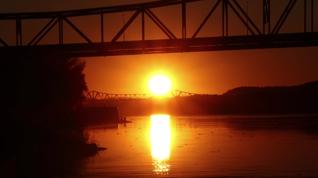 Dramatic orange sun sets between two bridges and reflects off of water