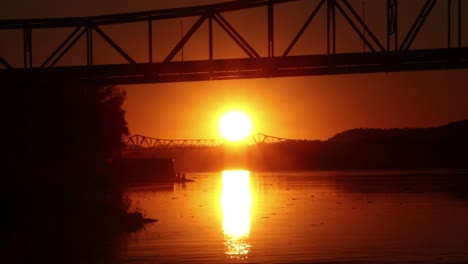 dramatic orange sun sets between two bridges and reflects off of water