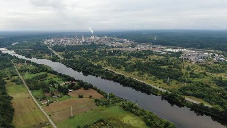 Cityscape-of-Jonava-and-chemical-industry-buildings-with-smoking-chimneys-in-horizon-during-light-rainstorm,-aerial-drone-view