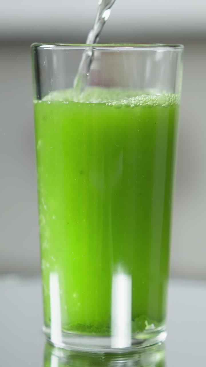 agua vertida en un vaso alto, mezclada con jugo verde, creando una bebida refrescante