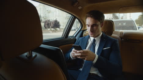 hombre de negocios agresivo escribiendo un mensaje enojado en el teléfono móvil en un coche moderno.