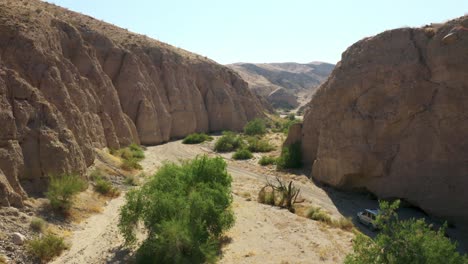 aerial: silver sedan driving through canyon in desert mountain terrain