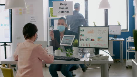 executive manager with face mask showing statistics to her collegue