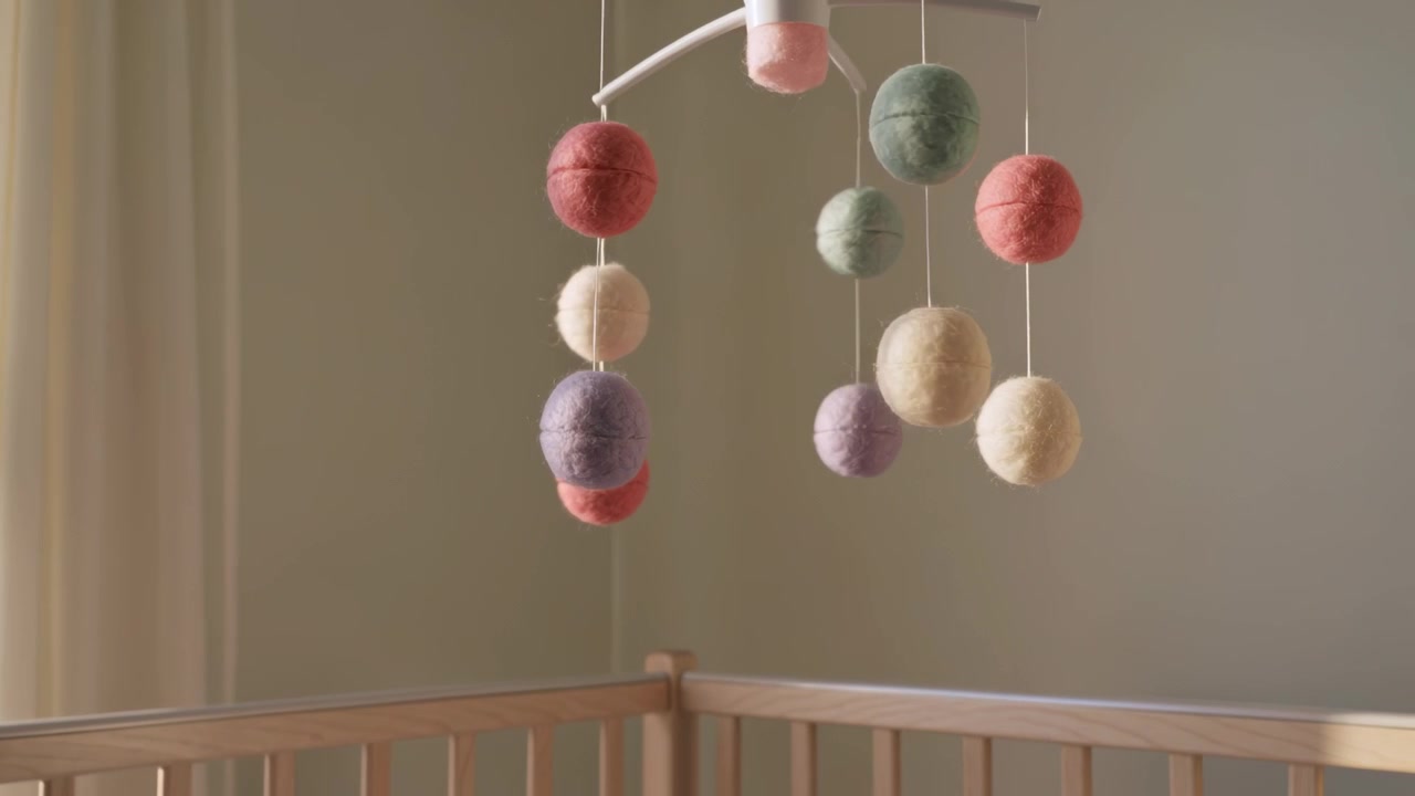 Rotating pastel felt ball mobile spinning over light wood crib corner, moving from window breeze