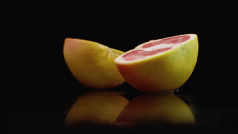 movimiento lento. pomelo jugoso con gotas y se rompe en 2 partes con salpicaduras en una mesa de vidrio con reflejo en un fondo oscuro.