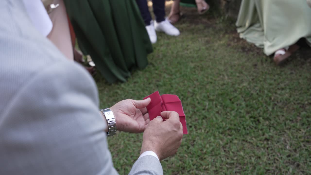 person holding a folded red cloth with a single gold ring on top, appearing as part of a magic or revealing trick