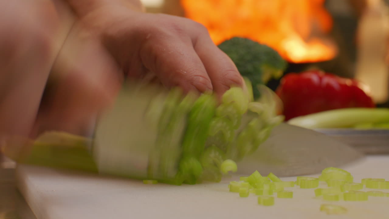 Close Up of Cook Slicing Fresh Celery with Sharp Knife on Kitchen Cutting Board