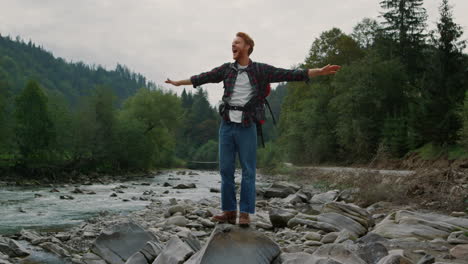 Positive-man-raising-hands-in-mountain-landscape.-Male-traveler-feeling-freedom