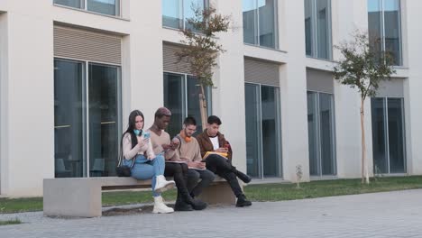 mulitcultural students using their own mobile sitting in a bench outdoors
