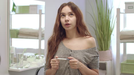 young woman holding pregnant test and waiting results in bath room interior.