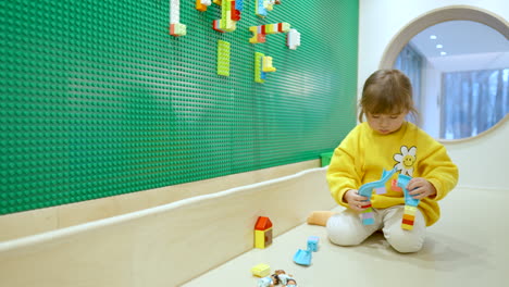 little girl playing with colorful lego blocks at indoor playroom - slow motion wide