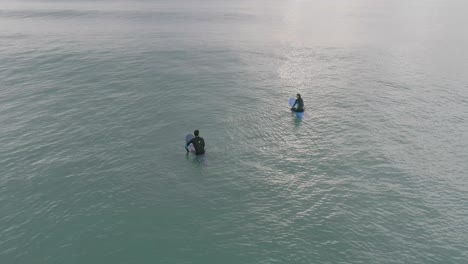 a couple of surfers chat while waiting for waves sitting on their surfboards during an early morning surf session.