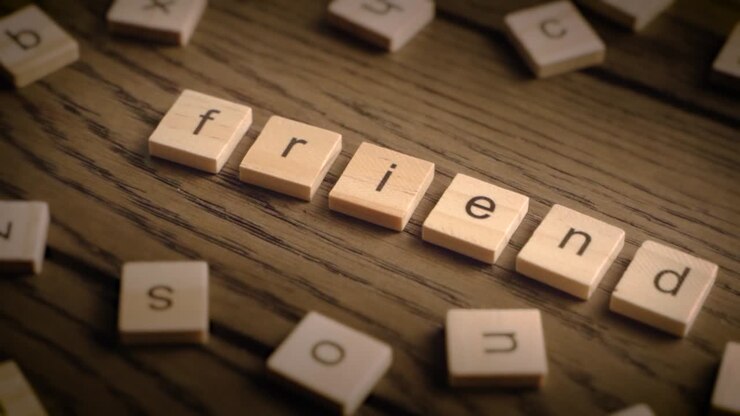 Tessere di Scrabble in legno compongono la parola "amico" mentre la telecamera effettua una panoramica su una superficie di legno rustica in una luce calda.