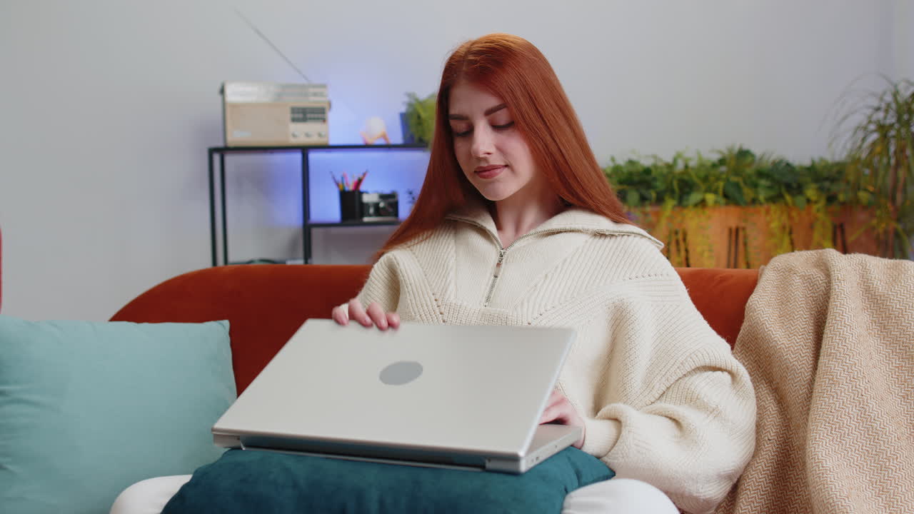 mujer joven independiente sentada en el sofá cerrando la computadora portátil después de terminar el trabajo en la habitación en casa