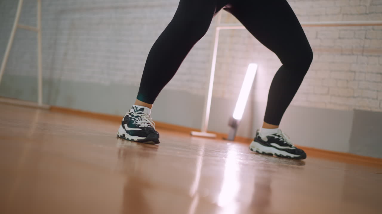 Leg view of woman in black leggings and sneakers moving up and down during energetic dance routine on polished studio floor showing rhythm movement coordination and athletic motion