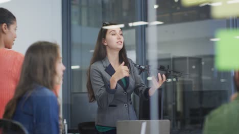 mujer caucásica con un avión no tripulado dando una presentación a un grupo diverso de colegas