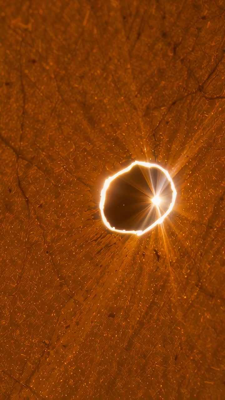 Vertical video: Moving light causing central circular hole showing starburst glowing rim at macro